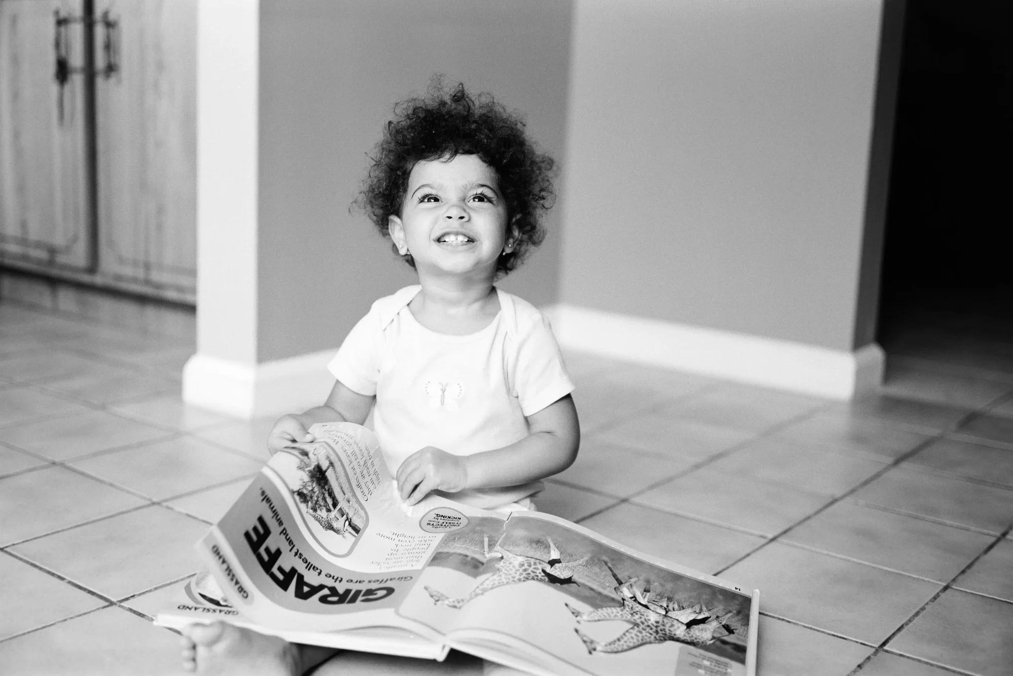 Criança sorrindo sentada no chão com um livro aberto